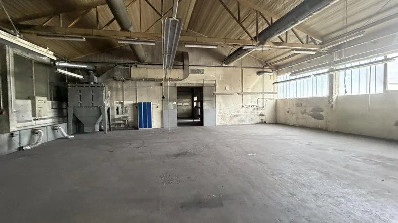 Große, leere Lagerhalle mit hohen Decken und sichtbaren Dachbalken, bereit für neue Nutzung.