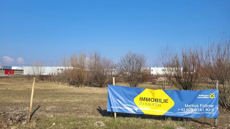 Blick auf ein unbebautes Grundstück mit einem 'Immobilie zu kaufen'-Banner unter klarem blauem Himmel.