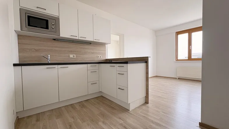 Helle, offene Wohnküche mit weißer Einbauküche, Mikrowelle und Laminatboden.