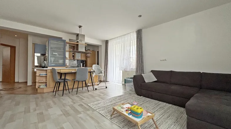 Heller offener Wohnbereich mit integrierter Küche, Laminatboden und Zugang zum Balkon.