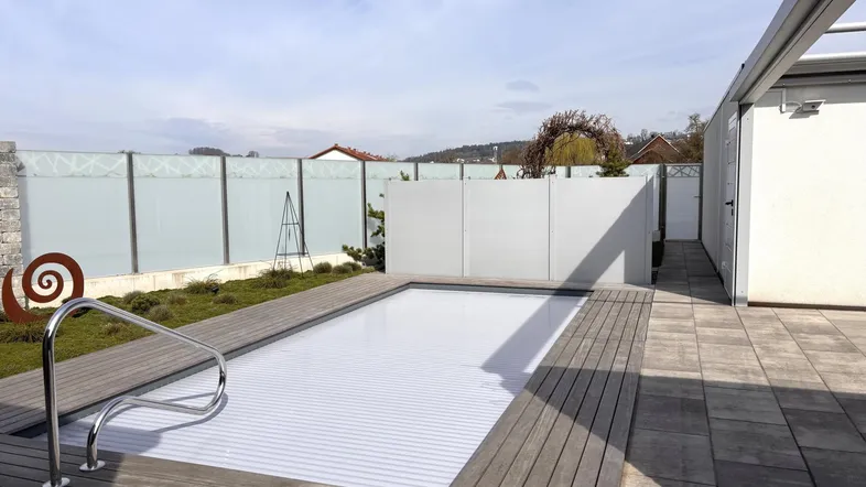 Moderner Außenbereich mit überdachtem Pool, Holzdeck und Sichtschutzwand.