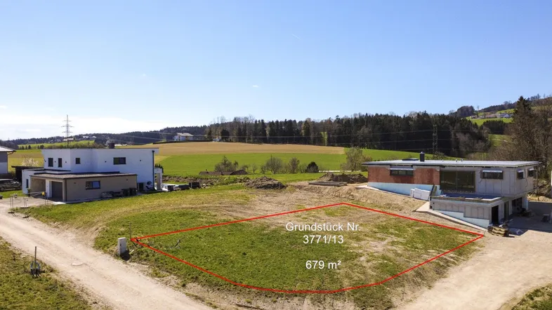 Luftaufnahme eines Baugrundstücks mit roter Umrandung und umliegender ländlicher Landschaft.