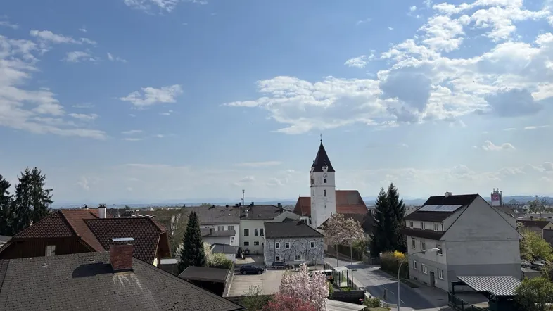 Panoramablick über die Stadt mit Kirchturm und umliegender Landschaft unter blauem Himmel.
