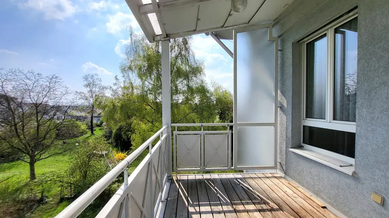 Heller Balkon mit Holzboden und Blick ins Grüne, ideal zum Entspannen im Freien.