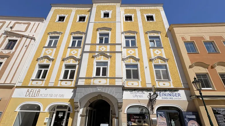 Historische Fassade eines Gebäudes mit gelbem Putz, vielen Fenstern und einem markanten Torbogen.