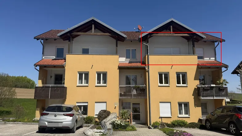 Gelbe Fassade eines Mehrfamilienhauses mit Balkonen und Satteldach.