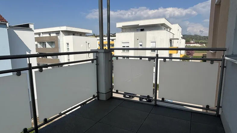 Balkon mit Fliesenboden, Milchglasgeländer und Blick auf moderne Wohngebäude.