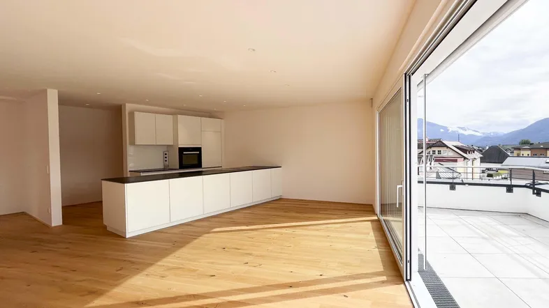 Helles, offenes Wohnzimmer mit integrierter Küche, Holzboden und Zugang zu einer großen Terrasse mit Bergblick.
