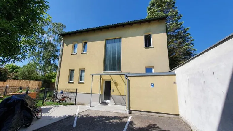 Mehrfamilienhaus mit gelber Fassade, großen Fenstern und Parkplätzen im Freien.