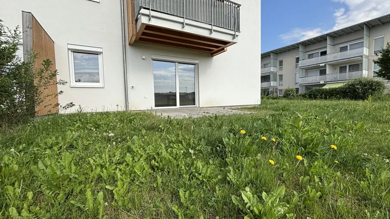 Neubauwohnung mit Balkon und Zugang zu einer kleinen Grünfläche im Freien.