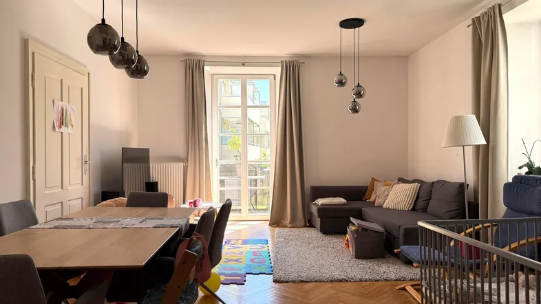 Heller Wohn- und Essbereich mit Fischgrätparkett, großem Esstisch und Zugang zum Balkon.