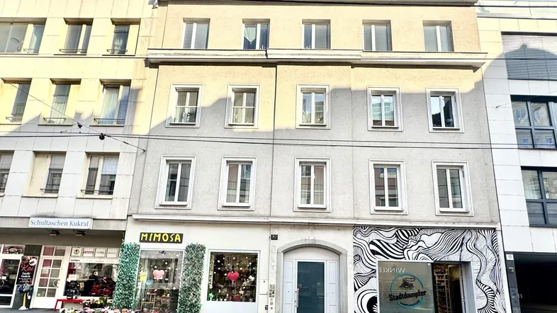 Mehrstöckiges Gebäude mit Geschäften im Erdgeschoss und Wohnungen darüber in einer städtischen Umgebung.