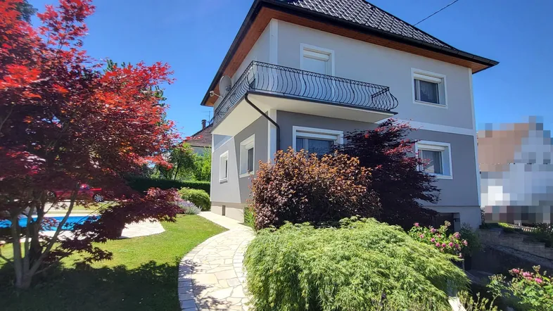 Hausansicht mit Garten, Pool und rotem Ahornbaum unter blauem Himmel.