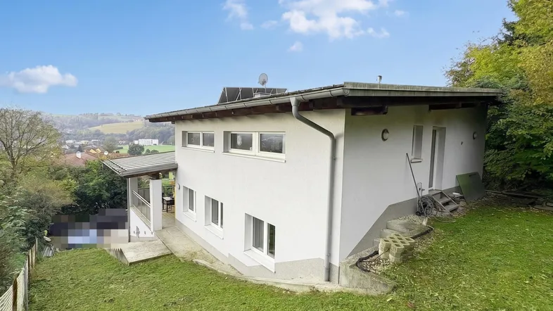 Weißes Einfamilienhaus mit Satteldach, umgeben von einem grünen Garten und weitem Blick über die Landschaft.