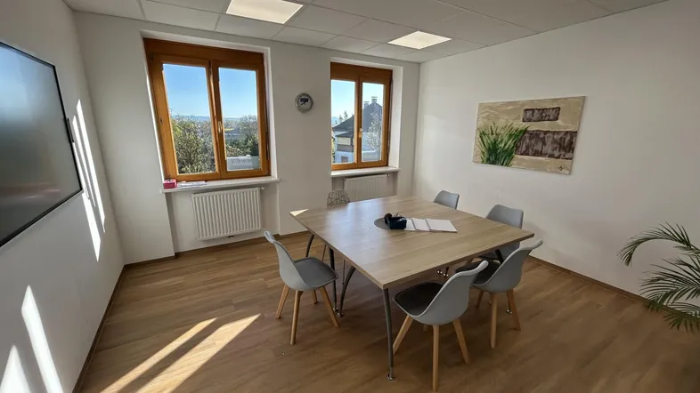 Heller Büroraum mit Holzboden, großem Tisch und Stühlen, ideal für Besprechungen oder als Arbeitsplatz.