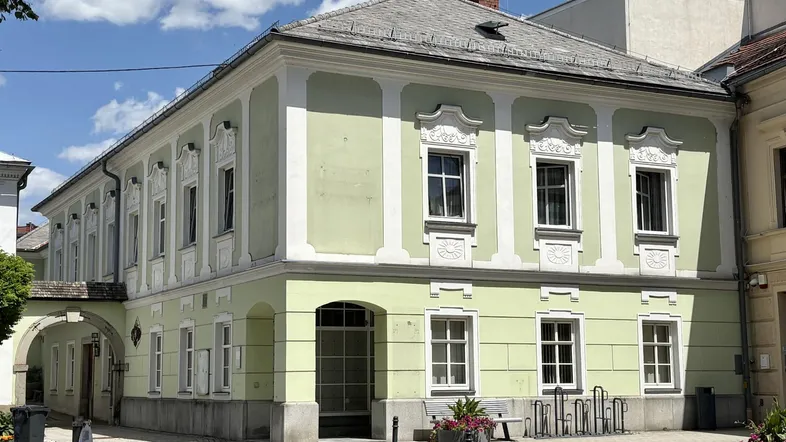 Historisches Gebäude mit hellgrüner Fassade und dekorativen Fensterrahmen an einem sonnigen Tag.