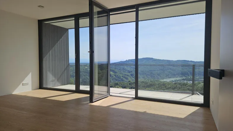 Heller Wohnraum mit Holzboden und großen Fenstern, die einen weiten Blick auf die Natur bieten.