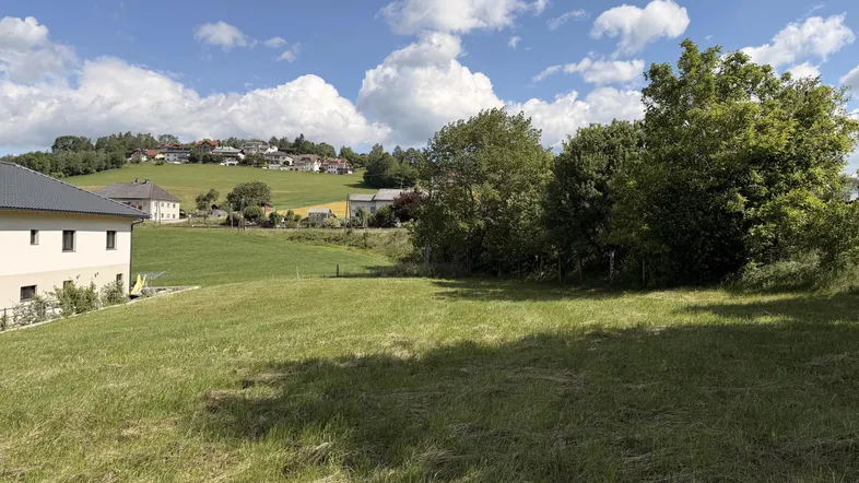 Weitläufiges grünes Grundstück mit Blick auf die umliegende Landschaft und Häuser auf einem Hügel.