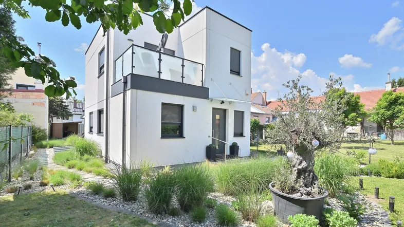 Moderne Hausfassade mit gepflegtem Vorgarten und dekorativen Pflanzen unter blauem Himmel.