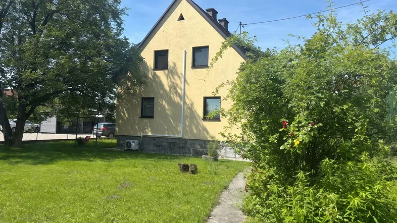 Gelbes Einfamilienhaus mit Satteldach und grünem Garten unter blauem Himmel.