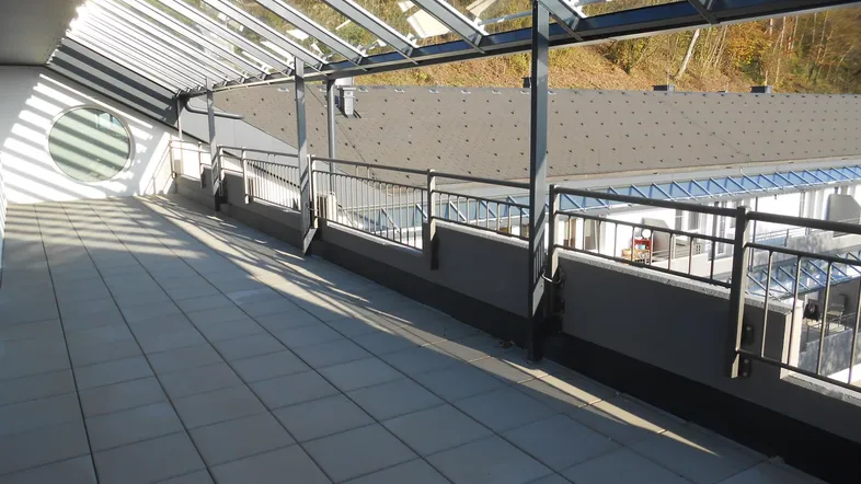 Große, geflieste Terrasse mit Glasdach und Blick auf die Umgebung und Bäume.