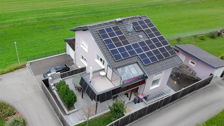 Luftaufnahme eines gepflegten Einfamilienhauses mit Solaranlage auf dem Dach, Garten und Terrasse, umgeben von grünen Feldern.