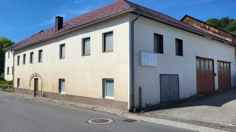 Gebäudeansicht von der Straße mit Putzfassade und Garagentoren. Das Dach ist mit roten Ziegeln gedeckt.