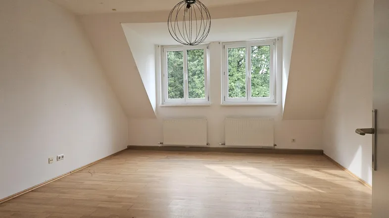 Geräumiges Zimmer im Dachgeschoss mit Holzboden, großen Fenstern und schräger Decke.