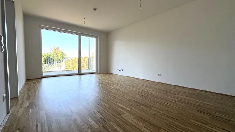 Helles Zimmer mit Holzboden und großer Glasfront, die Zugang zu einem Balkon bietet.
