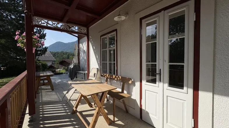 Gemütliche überdachte Terrasse mit Holztisch und Stühlen, ideal für Mahlzeiten im Freien mit Bergblick.