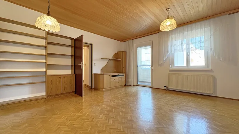 Geräumiges Wohnzimmer mit Holzdecke, Fischgrätparkett und Zugang zu einem Balkon.