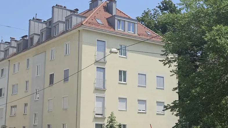 Mehrstöckiges Wohngebäude mit heller Fassade, roten Ziegeldächern und kleinen Balkonen.