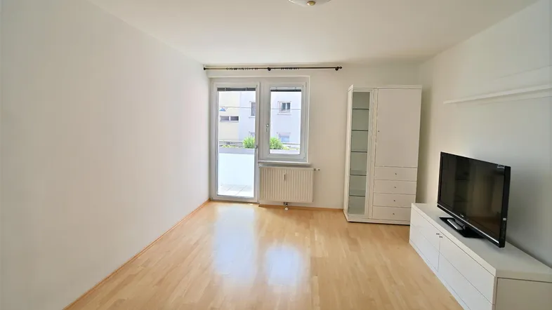 Helles Wohnzimmer mit Parkettboden, Balkonzugang und weißem TV-Möbel.