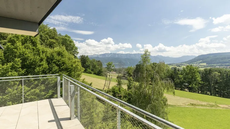 Geräumiger Balkon mit Fliesenboden und weitem Blick über grüne Landschaft, See und Berge.