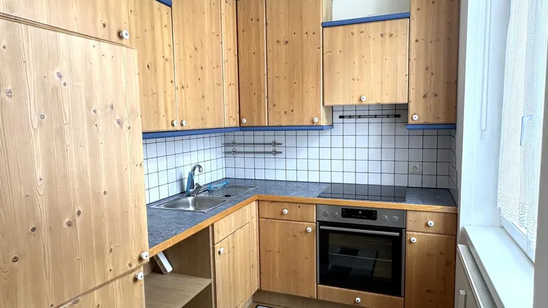Funktionale Küche mit Holzschränken, Fliesenrückwand und integrierten Elektrogeräten.