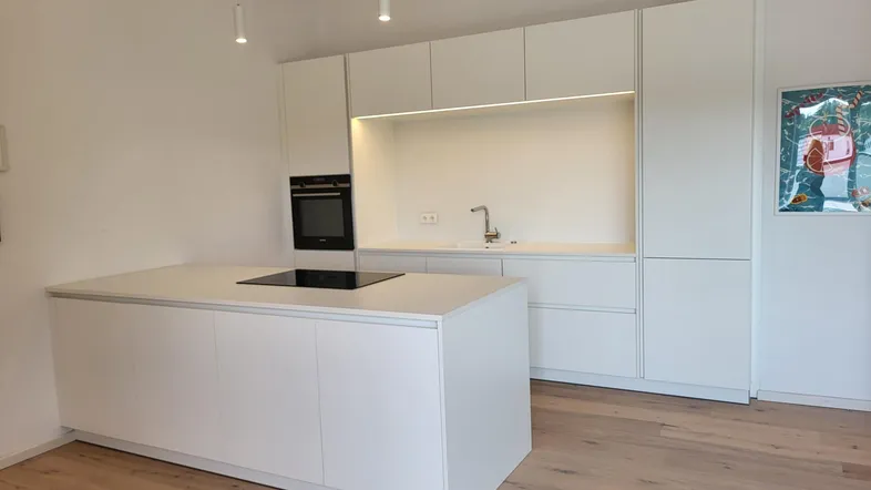 Moderne, helle Küche mit weißer Kücheninsel, integriertem Kochfeld und Backofen.