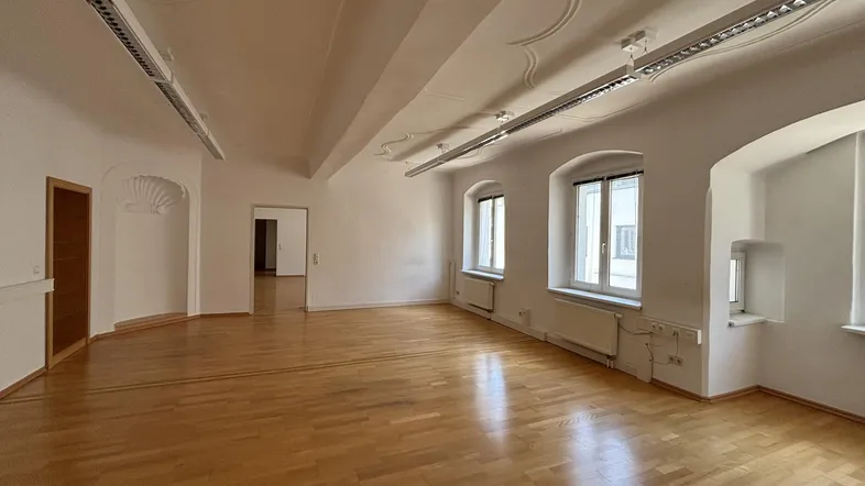 Geräumiger, leerer Büroraum mit hohen Decken, Holzboden und großen Fenstern, die viel Tageslicht hereinlassen.