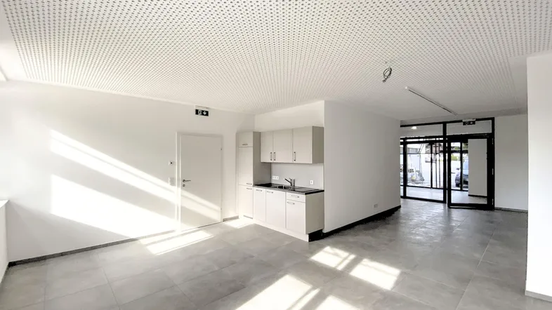 Großer, heller Raum mit moderner Küchenzeile, grauen Fliesen und perforierter Akustikdecke, ideal für Büro oder Gewerbe.