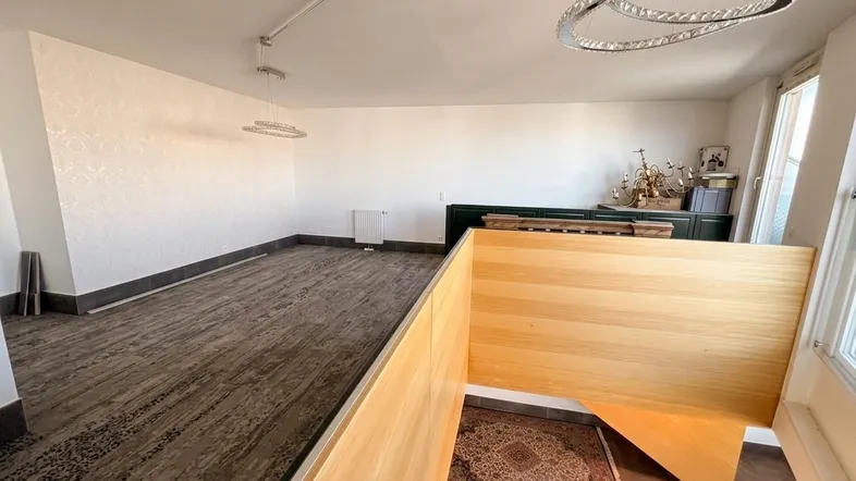 Geräumiger Wohnbereich mit gemusterter Akzentwand, dunklem Bodenbelag, moderner Deckenleuchte und Holzabtrennung.