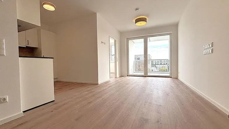 Helles Wohnzimmer mit Holzboden und Zugang zu einem Balkon, offen gestaltet und modern.