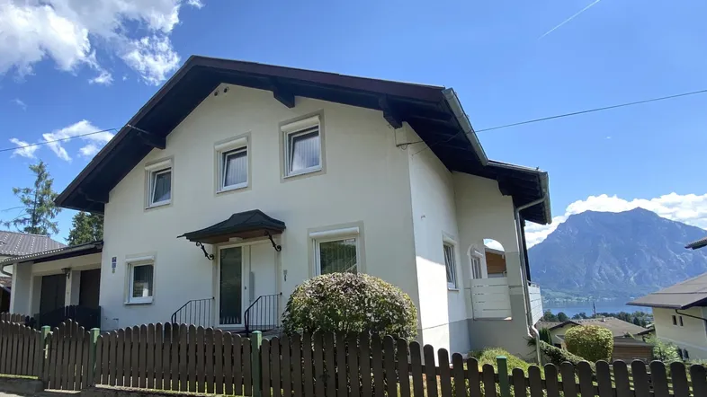 Gepflegte Hausfassade mit Blick auf den See und die umliegende Berglandschaft unter blauem Himmel.