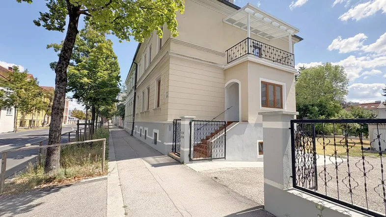 Ansicht der Gebäudefassade mit Balkon und Zugang zum Eingangsbereich von der Straße aus.