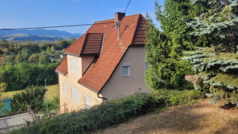 Hausfassade mit Ziegeldach und Blick auf die umliegende Landschaft unter blauem Himmel.