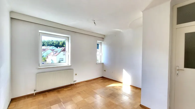 Heller Wohnraum mit Fischgrätparkettboden, weißen Wänden und zwei Fenstern für viel Tageslicht.
