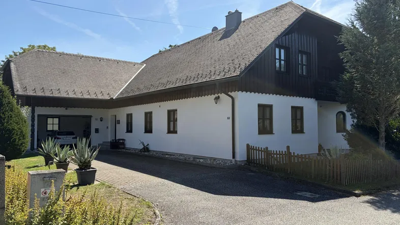 Traditionelles Einfamilienhaus mit weißer Fassade, Satteldach und überdachtem Carport.