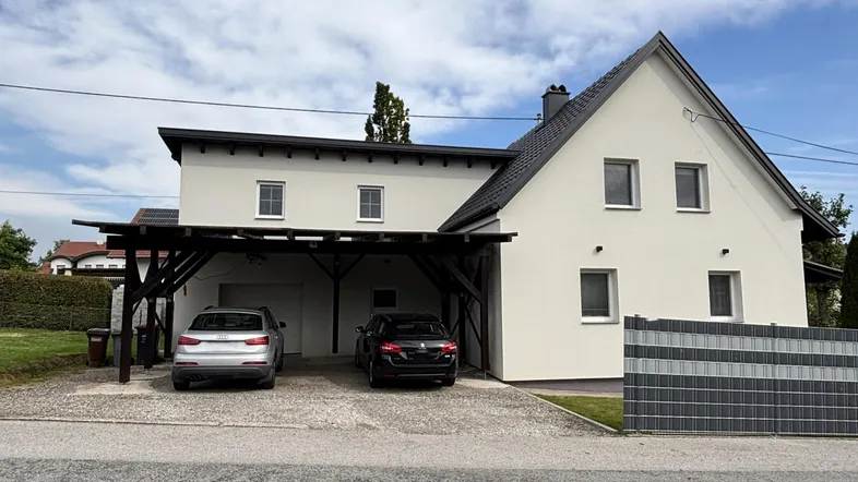 Modernes Einfamilienhaus mit weißer Fassade, Sattel- und Flachdach sowie einem Carport mit Solaranlage.