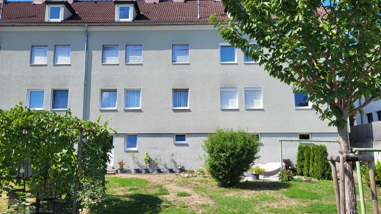 Rückseite des Gebäudes mit einem gepflegten Gartenbereich und einer grünen Pergola.