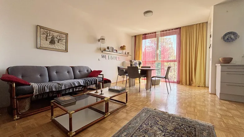 Helles Wohn- und Esszimmer mit Parkettboden, Sofa und Esstisch, sowie Zugang zum Balkon.