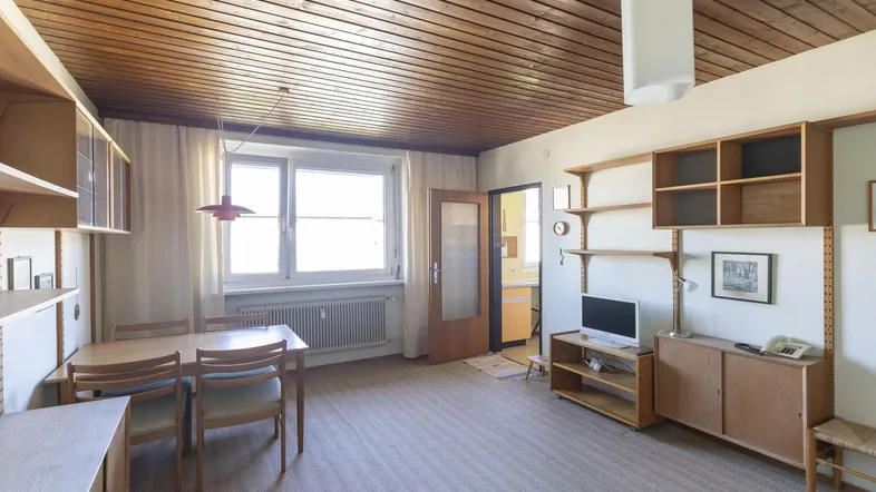 Geräumiger Wohn-Essbereich mit Holzbalkendecke, Teppichboden und Zugang zur Küche.