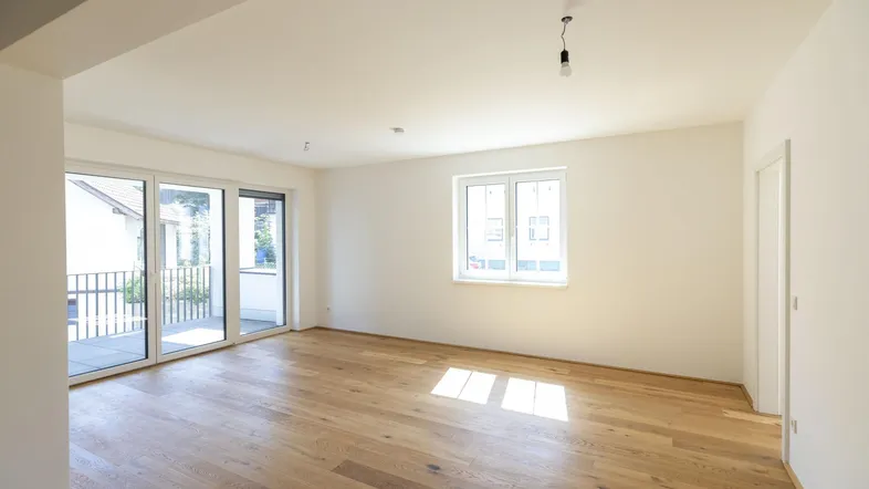 Helles Wohnzimmer mit Holzboden und Zugang zu einem Balkon, ideal für entspannte Stunden.